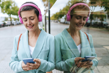 Frau in Jacke, die mit ihrem Handy Musik hört - KIJF02436