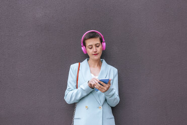 Frau in Jacke, die mit ihrem Handy Musik hört - KIJF02437