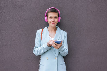 Woman dressed in jacket listening to music with her mobile phone - KIJF02438