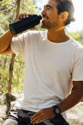Männlicher Wanderer trinkt Wasser, während er auf einem Felsen im Wald sitzt - CAVF63165