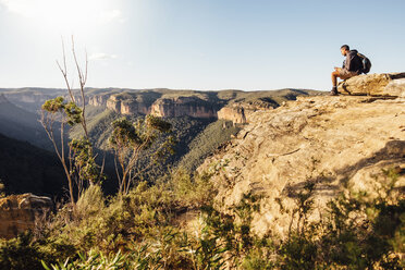 Seitenansicht eines Wanderers mit Rucksack auf einem Berg sitzend gegen den Himmel an einem sonnigen Tag - CAVF63169