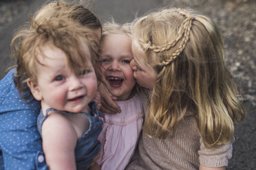 Hohe Winkel Ansicht der glücklichen niedlichen Mädchen küssen Schwester, während auf der Straße im Wald sitzen - CAVF63189