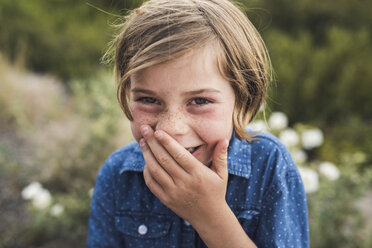 Close-up portrait of happy girl with hand covering mouth standing in forest - CAVF63200