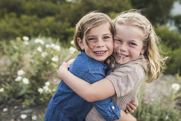 Portrait of happy sisters embracing while standing against plants in forest - CAVF63201