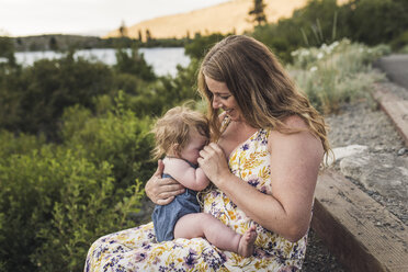 Mother breastfeeding daughter while sitting on steps against plants in forest - CAVF63208