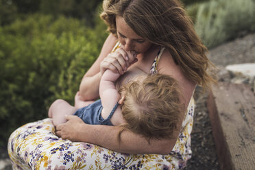 Mother breastfeeding daughter while sitting against plants in forest - CAVF63209