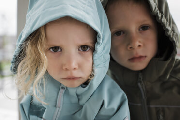 Close-up portrait of siblings in raincoats standing at home - CAVF63225