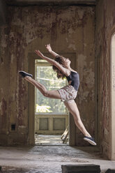 Side view of young woman leaping while practicing ballet in old building - CAVF63257