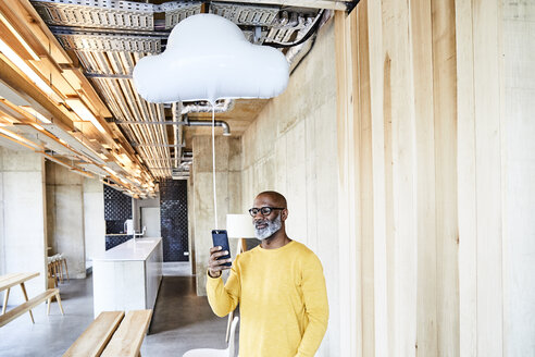 Mature businessman holding cell phone attached to cloud balloon - FMKF05445