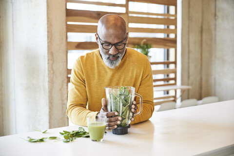 Älterer Geschäftsmann im Büro bereitet einen Smoothie zu, lizenzfreies Stockfoto