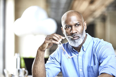 Mature businessman in office thinking with cloud balloon in background - FMKF05493