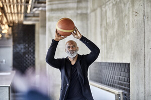 Älterer Geschäftsmann spielt Basketball in einem modernen Büro - FMKF05505