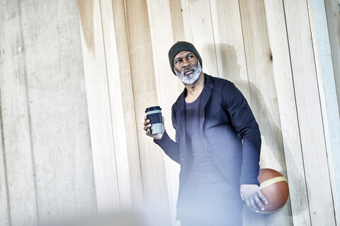 Älterer Geschäftsmann mit Kaffee zum Mitnehmen und Basketball an einer Holzwand, lizenzfreies Stockfoto