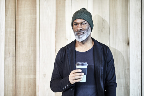 Porträt eines selbstbewussten reifen Geschäftsmannes mit Kaffee zum Mitnehmen an einer Holzwand, lizenzfreies Stockfoto