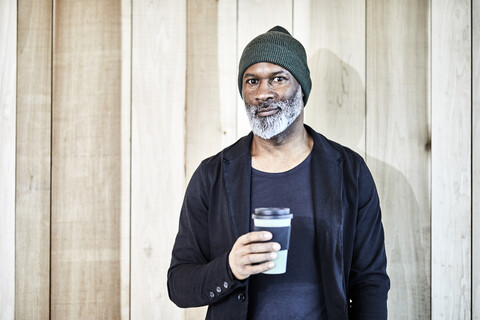 Portrait of confident mature businessman with takeaway coffee at wooden wall stock photo