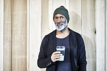 Porträt eines selbstbewussten reifen Geschäftsmannes mit Kaffee zum Mitnehmen an einer Holzwand - FMKF05507