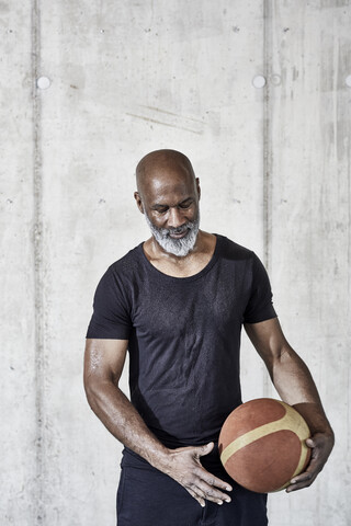 Älterer Mann hält Basketball an Betonwand, lizenzfreies Stockfoto