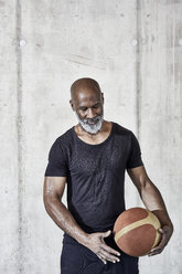 Mature man holding basketball at concrete wall - FMKF05512