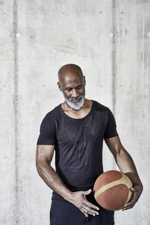 Älterer Mann hält Basketball an Betonwand - FMKF05512