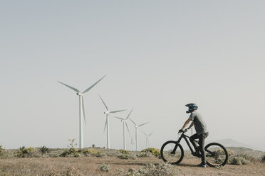 Spanien, Lanzarote, Mountainbiker auf einem Ausflug in Wüstenlandschaft mit Windkraftanlagen im Hintergrund - AHSF00078