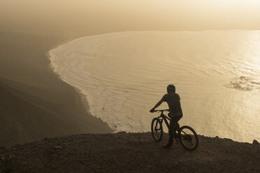 Spanien, Lanzarote, Mountainbiker auf einem Ausflug an der Küste bei Sonnenuntergang genießen die Aussicht - AHSF00105