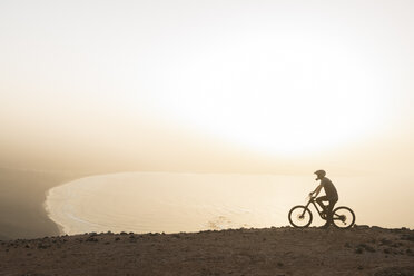 Spanien, Lanzarote, Mountainbiker bei einem Ausflug an der Küste bei Sonnenuntergang - AHSF00109