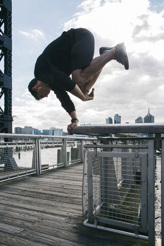 USA, New York, Brooklyn, young man doing Parkour handstand on railing of pier in front of Manhattan skyline stock photo