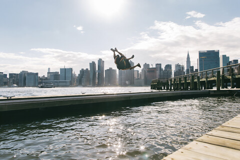 USA, New York, Brooklyn, two young men doing backflip on pier in front of Manhattan skyline stock photo