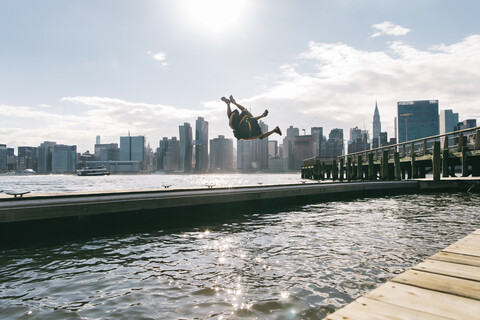 USA, New York, Brooklyn, zwei junge Männer machen einen Rückwärtssalto auf einem Pier vor der Skyline von Manhattan, lizenzfreies Stockfoto