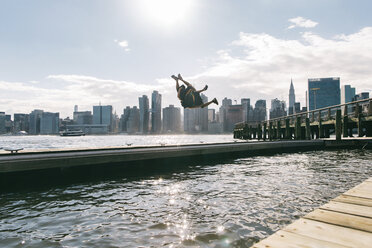 USA, New York, Brooklyn, zwei junge Männer machen einen Rückwärtssalto auf einem Pier vor der Skyline von Manhattan - JUBF00338
