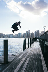 USA, New York, Brooklyn, junger Mann beim Parkour-Sprung von der Holzstange vor der Skyline von Manhattan - JUBF00339