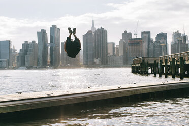 USA, New York, Brooklyn, junge Männer machen Rückwärtssalto auf dem Pier vor der Skyline von Manhattan - JUBF00341