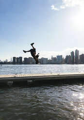 USA, New York, Brooklyn, young man doing backflip on pier in front of Manhattan skyline - JUBF00342