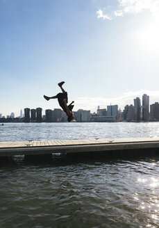 USA, New York, Brooklyn, junger Mann macht Rückwärtssalto auf dem Pier vor der Skyline von Manhattan - JUBF00342