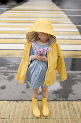 Mädchen in gelber Regenjacke, auf einem Zebrastreifen stehend, mit Flieder in der Hand - EYAF00014