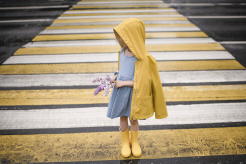 Girl wearing yellow rainjacket, standing on zebra crossing, holding lilac - EYAF00015