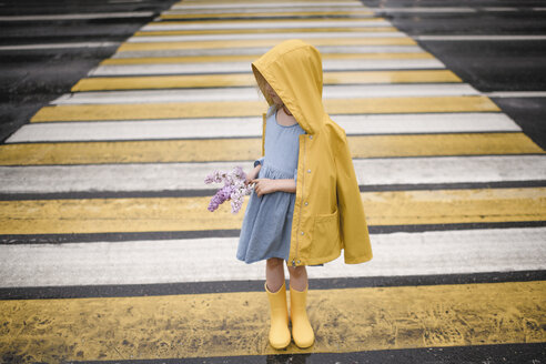 Mädchen in gelber Regenjacke, auf einem Zebrastreifen stehend, mit Flieder in der Hand - EYAF00015