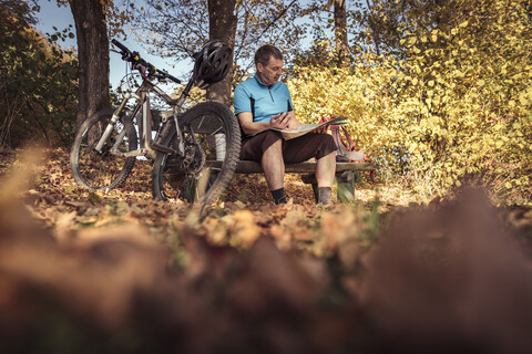 Mann mit Mountainbike sitzt auf einer Bank und studiert eine Karte, lizenzfreies Stockfoto