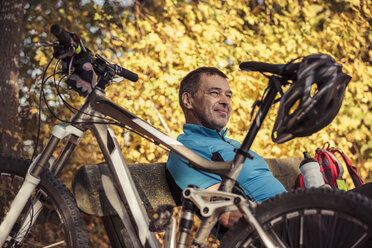 Man with mountainbike having a break sitting on a bench - SEBF00061