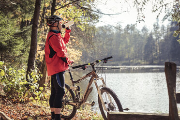 Man with mountainbike having a break at a lake in forest - SEBF00072