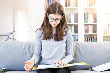 Portrait of girl sitting on the couch at home learning for school - LVF07881