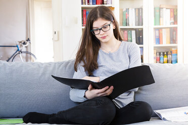 Portrait of girl sitting on the couch at home learning for school - LVF07882