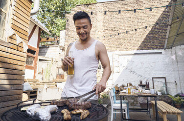 Junger Mann bereitet Fleisch auf einem Grill in einem Hinterhof zu - PDF01803