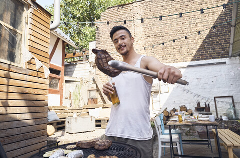 Junger Mann bereitet Fleisch auf einem Grill in einem Hinterhof zu, lizenzfreies Stockfoto