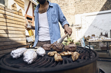 Junger Mann bereitet Fleisch auf einem Grill in einem Hinterhof zu - PDF01811