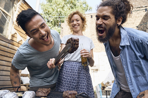 Friends having a barbecue n the backyard, preparing meat on a grill stock photo