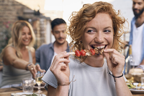 Junge Frau isst Fleischspieß in einer Hinterhof-Patisserie mit Freunden, lizenzfreies Stockfoto