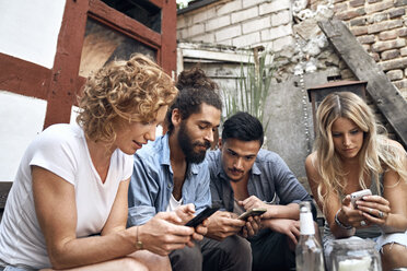 Friends sitting in a backyards, using smartphones - PDF01874