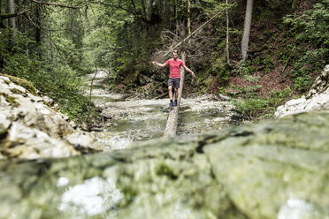 Germany, Bavaria, Upper Bavaria, lake Walchen, young man is crossing a torrent on a tree trunk - WFF00055