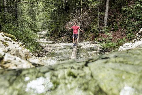 Deutschland, Bayern, Oberbayern, Walchensee, junger Mann überquert einen Wildbach auf einem Baumstamm - WFF00055